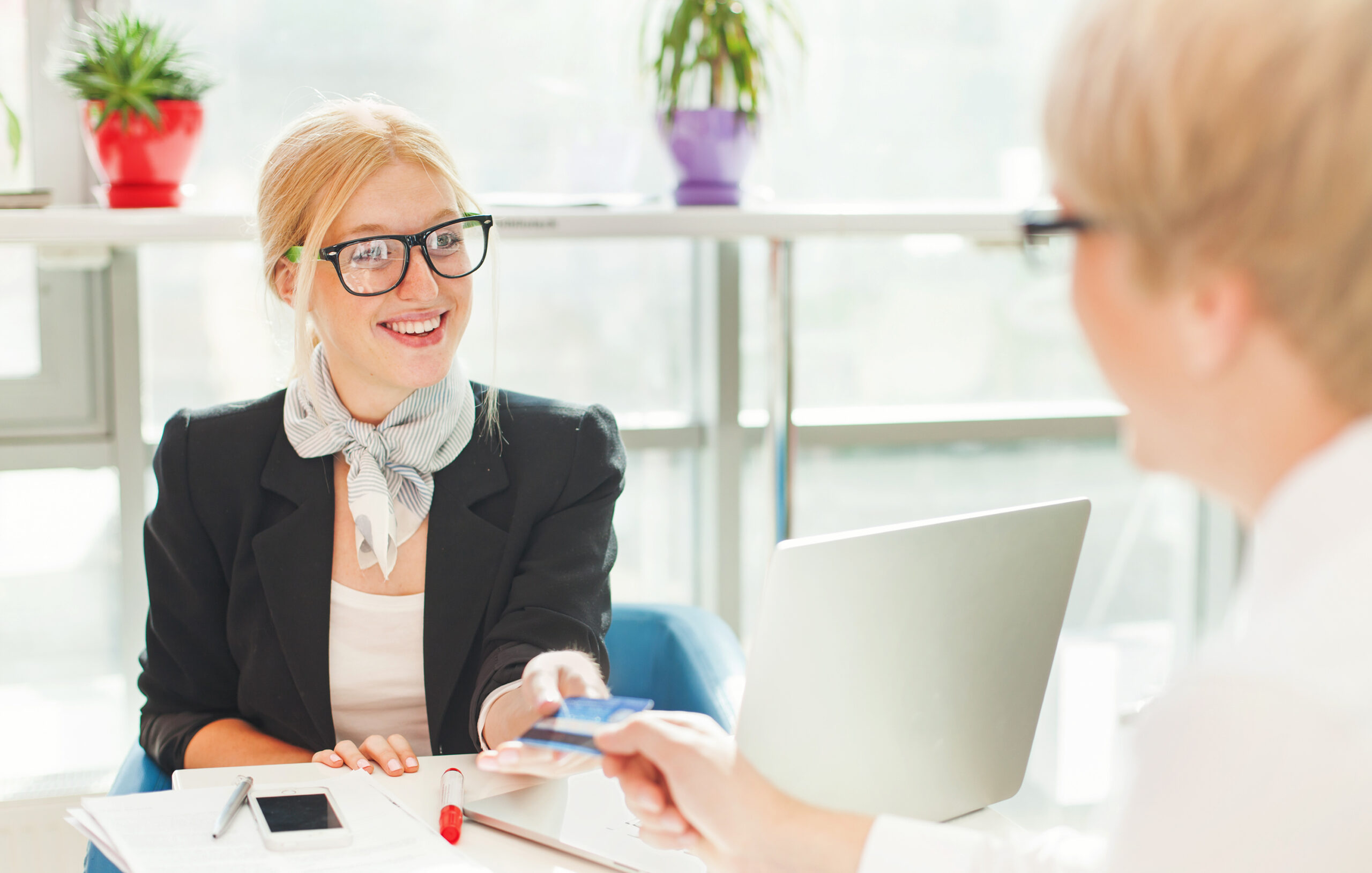 Woman handing credit card to another woman sitting behind a laptop