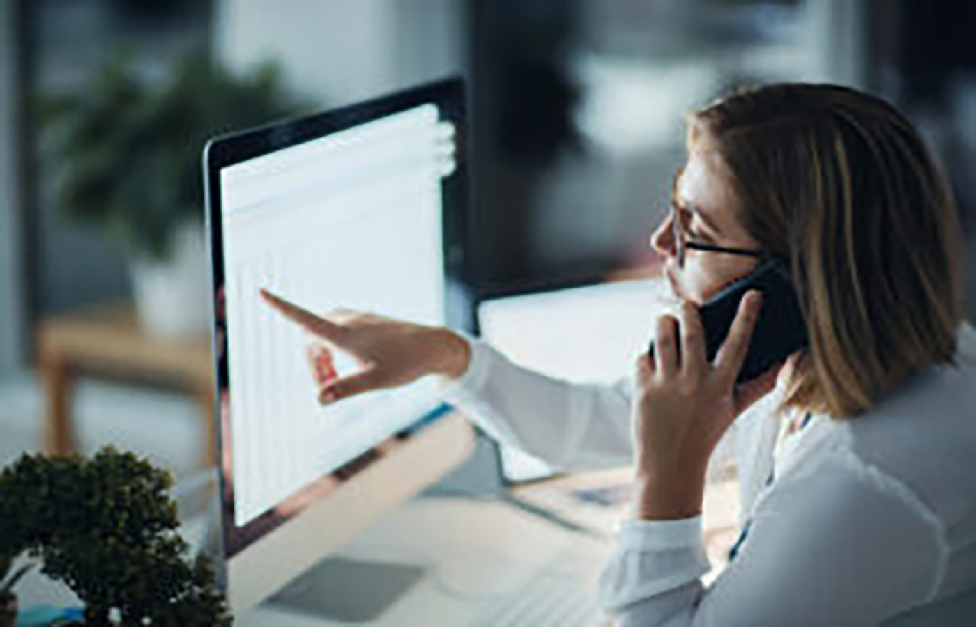 Woman sitting in front of computer monitor and pointing